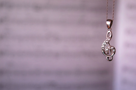 A treble clef pendant necklace dangling in front of sheet music.の写真素材
