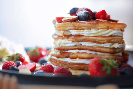 Pouring syrup over the pancakes with  forrest fruit stack of pancakes on the kitchen tableの写真素材