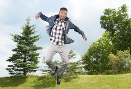 Teenager jumping in the air on a green hill with treesの写真素材
