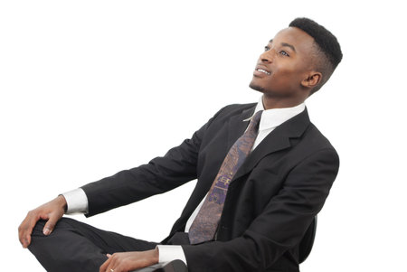 young man seated on chain staring up wearing black suit and tie