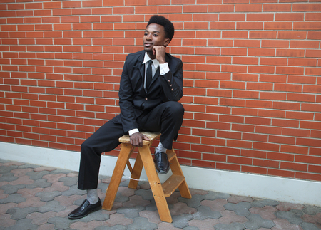 businessman thinking sitting wearing suit and tie brick wall outsideの写真素材