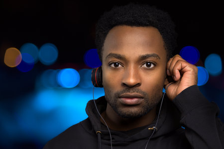 man holding headphones with one hand listening to music blue bokeh lights backgroundの写真素材