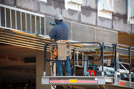 A construction worker on a cherry picker lift installing concrete panels on a building under...
