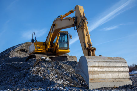 Heavy-duty excavator on a gravel mound at a construction site, industrial work, earthmoving shovel and development under a clear blue sky.の写真素材