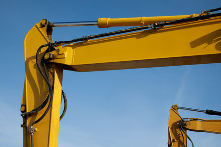 Close-up of two excavator arms showing hydraulic hoses, metal joints, and industrial wear,...