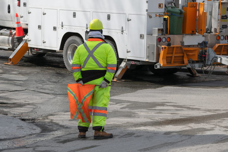 Construction worker wearing reflective safety clothing and helmet holding an orange traffic sign...