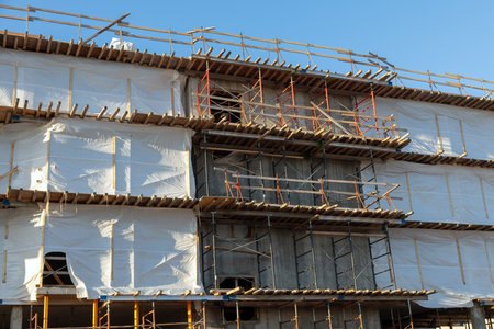 Facade of a modern building under construction featuring metal beams, scaffolding, and protective...