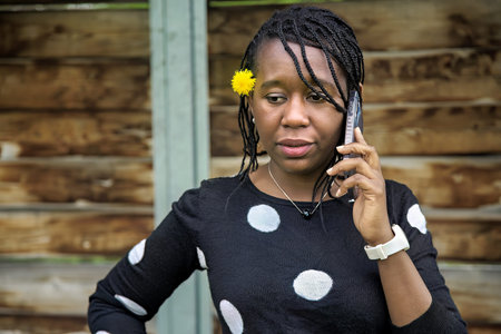African woman with braided hair and yellow flower in her hair talking on a mobile phone while...