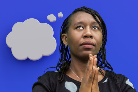 Thoughtful African American woman in prayer pose with hands together and thought bubble. Perfect for spirituality, meditation, hope, faith, contemplation and personal reflection concepts.の写真素材