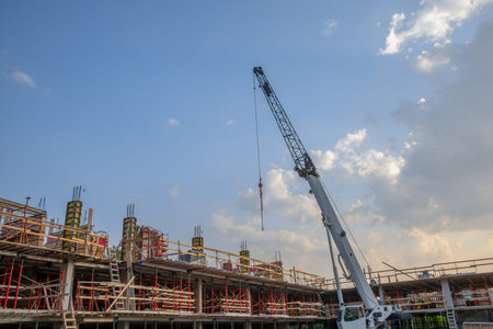 Active construction site with tower crane and concrete building structure with scaffolding. Modern...