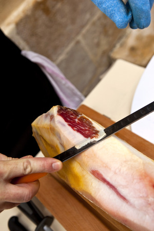 Cook cutting slice of ham in a kitchenの写真素材