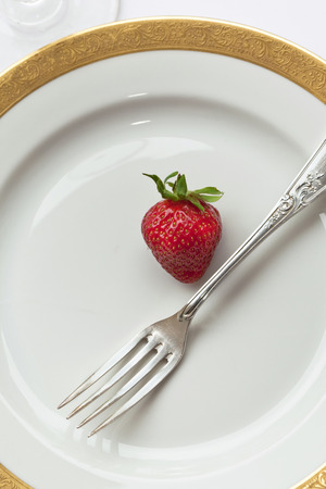 Strawberry and silver fork on a porcelain plateの写真素材