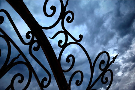 Close up of a wrought iron gate and cloudy sky on background