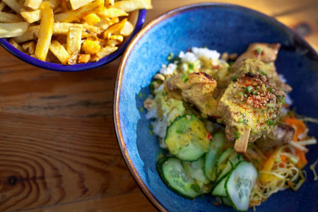 Chicken skewer and vegetables in a bowl with French fries on background