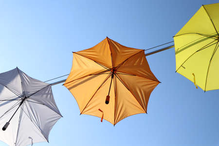 orange, white and yellow umbrellas hanging against clear blue skyの写真素材