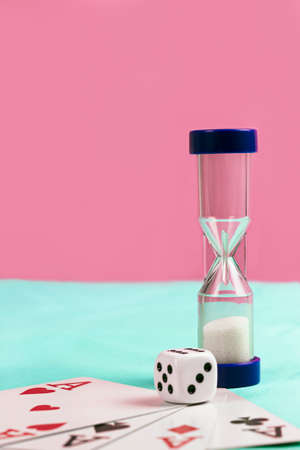 Playing Cards with Blue Sand Timer and Die on Blue and Pink Backgroundの写真素材