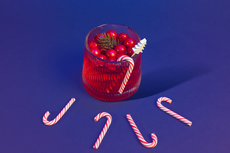 Vibrant Christmas Cranberry Cocktail Beverage in a Glass and Classic Red-White Candy Canes Arrangement on a Blue Backdropの写真素材