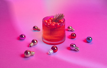 A Christmas Cranberry Cocktail Beverage in a Glass, Ornament Decorations, on a Pink & Red Holiday Background, Christmas Party Conceptの写真素材