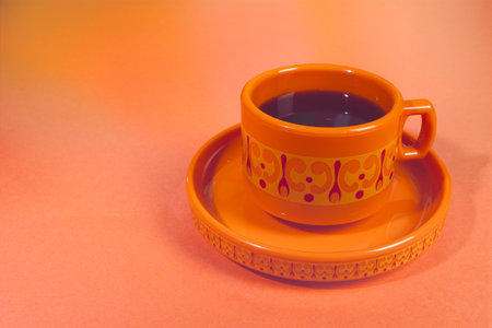 Vintage-Inspired Orange Cup and Saucer Set with Delicate Scrollwork Design on a Peach-Colored Surfaceの写真素材
