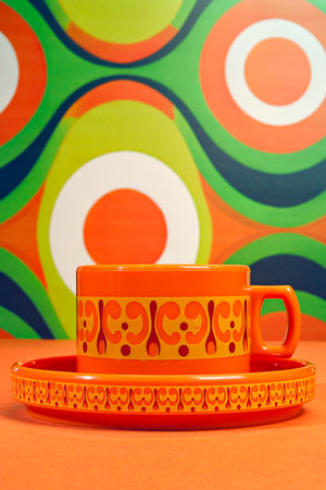 Vivid Orange and Funky Brown Patterned Coffee Cup Set against a Retro Wallpaper Designの写真素材