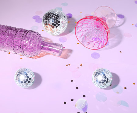 An After The Party Scene with Champagne Bottle Lying Down, A Tipped Over Coupe Glass, Confetti and Disco Balls on a Pastel Backgroundの写真素材