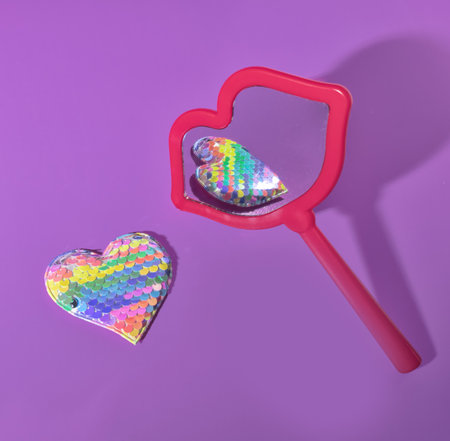 A Red Mouth Shaped Mirror Reflecting Rainbow Pastel Sequined Hearts for Valentine's Day on A Purple Backgroundの写真素材