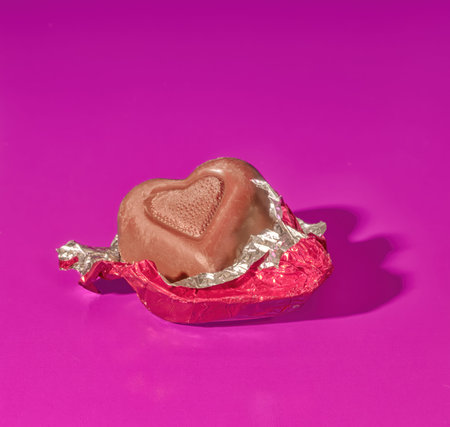 A Piece of Foil Covered Valentine's Day Milk Chocolate Candy on a Bright Pink Background