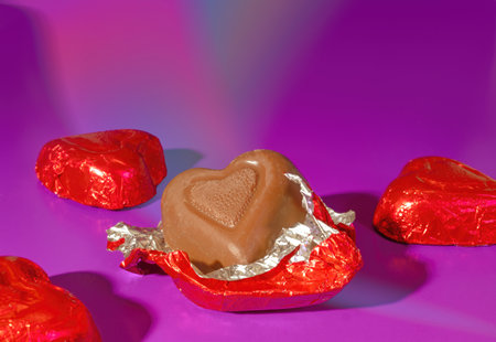 Four Pieces of Red Foil Covered Valentine's Day Milk Chocolate Candy on a Bright Pink Backgroundの写真素材