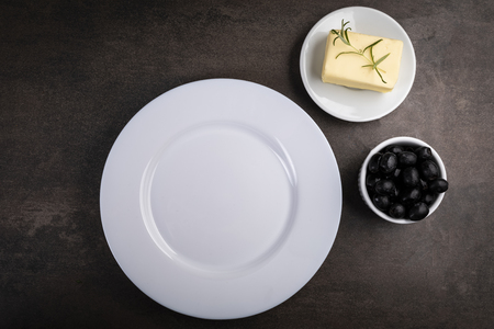 White empty plate, meal meal, olives and butter on a dark table. Horizontal frame, top view.の写真素材