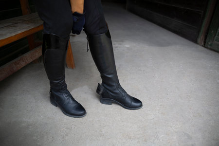 Stud, woman puts on professional leather riding boots.
