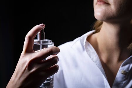 A woman in a white shirt is perfuming the skin of the neck. Dark backgroundの写真素材
