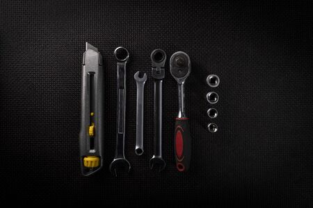 Set of chrome hand tools on a black background. Utility knife with segmented blade, combination wrenches with open and box ends and a socket set with a ratchet. Central, top view.の写真素材