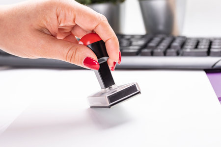 Woman stamps documents by plastic, rubber stamp, on a wooden, office desk. A traditional rubber ink...