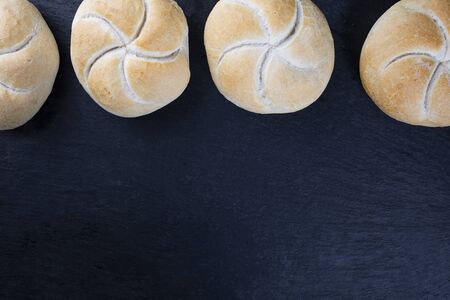 Freshly baked, crusty Kaiser rolls placed on a dark stone surface. Dark background, top view. A composition with text-space.の写真素材