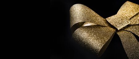 Deep black background with golden glitter shiny decorative gift bow with space for text. Christmas, new year, birthday, special occasions, luxury background.の写真素材