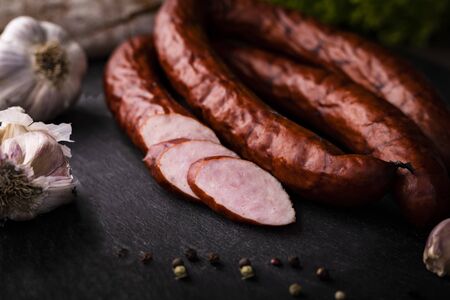Rustic composition of a traditional smoked sausage placed on a stony, black countertop with garlic and and pepper. Rings of tasty, homemade pork sausage.の写真素材