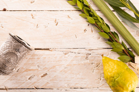 Composition of Jewish Sukkot festival symbols. The lulav - a set of four species: etrog, palm frond, myrtle and willow twigs and a kiddush cup on a light, wood background.の写真素材