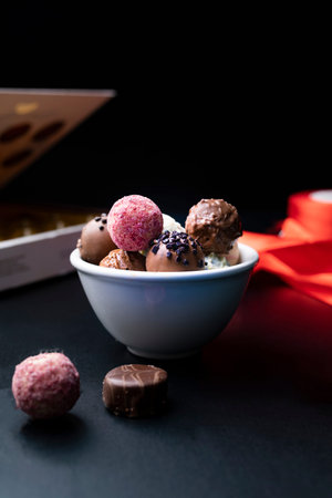 Bowl with delicious assorted chocolates with different toppings. Gourmet chocolates on a dark, stony...