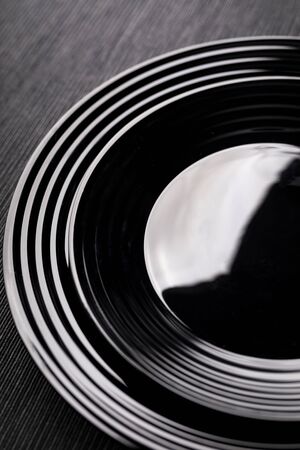 A table setting. A close-up of black plates of various sizes with a white rim on a dark wooden table. Modern tableware.の写真素材