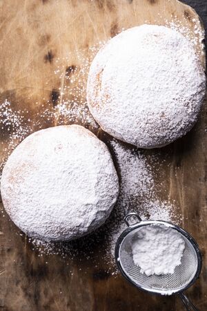 Donuts. Sweet carnival pastries, delicacy for Fat Thursday. Doughnuts covered with powdered sugar, sifter and scattered powdered sugar on the wooden cutting board. の写真素材