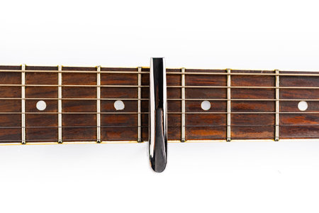 A fretboard of an acoustic guitar with strings and a capotasto, on a white background. A classical,...