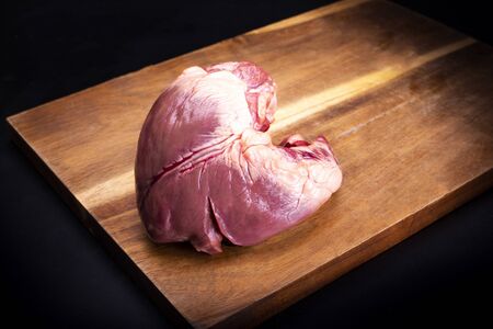 Pork heart on a wooden cutting board on a dark background.の写真素材