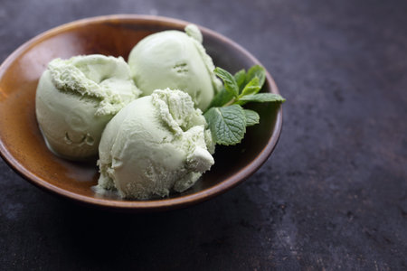 Close up of three scoops of green tea, pistachio, oriental ice cream decorated with mint leaf in a...