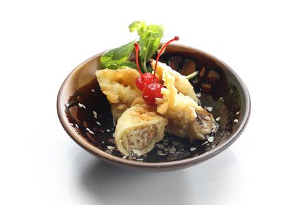 Fried banana in tempura with almond flakes and maraschino cherry on the top in a small, minimal-style, brown bowl decorated with melted chocolate. An oriental dessert isolated on a white background.の写真素材