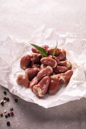 Chicken hearts, giblets decorated with bay leaves, salt and colorful peppercorns. Raw poultry hearts on a white paper on a gray stony worktop. Poultry parts. Source of iron. Iron rich foods.の写真素材