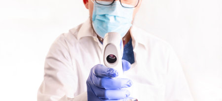 Doctor in gloves and face mask holding a infrared forehead thermometer, measuring body temperature....