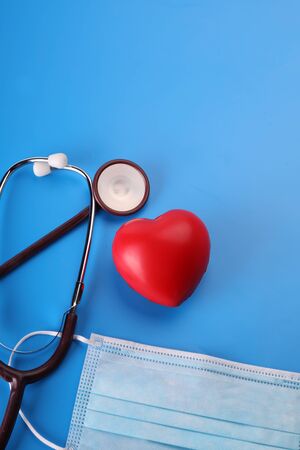 Medical concept. A single use, sterile surgical face mask, stethoscope and red heart on a vibrant blue background. Fighting against infections. Healthcare concept.の写真素材