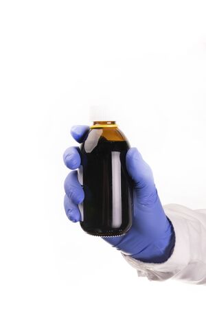 Medical worker, pharmacist hand with nitrile, blue, protective glove, holding a blank bottle of cough syrup. on a white background. Pharmaceuticals. Medicines in package. Diseases treatment.の写真素材