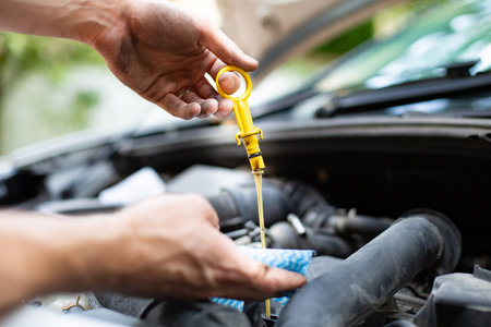 Male hand holding a dipstick under the hood of the car, side view. Checking car engine oil level....