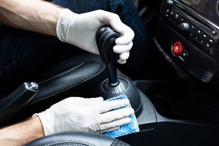Car SPA. Man in protective gloves cleaning a car interior with high quality car detailing cosmetics. Wiping down a gearstick and a center console. Auto detailing. Automobile interior preservation.の写真素材